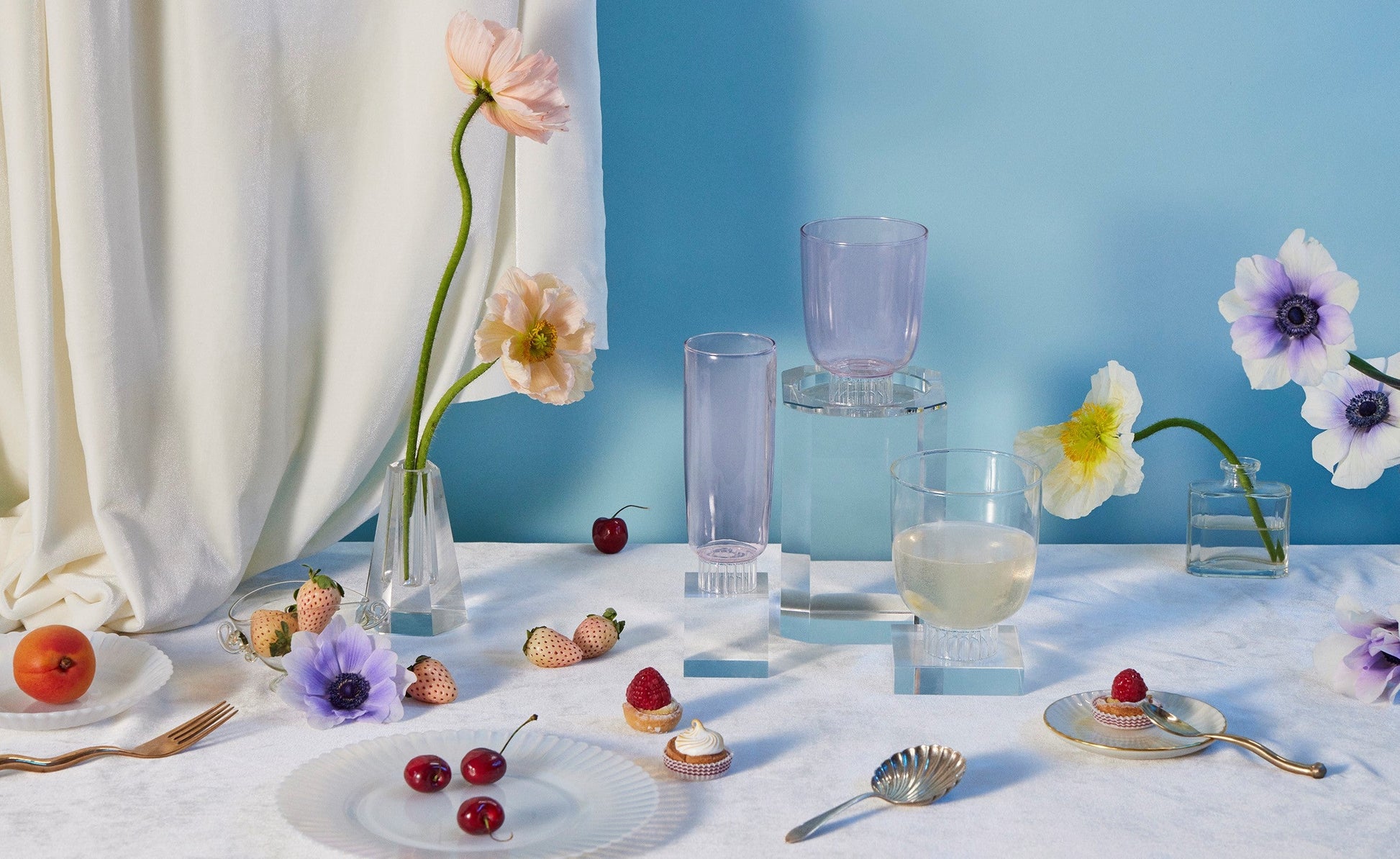Sprezz pink and clear safe glassware for champagne and flutes, scattered around a spring tablescape adorned with flowers, fruits, and small desserts. Colored champagne flutes and colored glass tumblers are perfect for toasting at a birthday party or easter brunch.