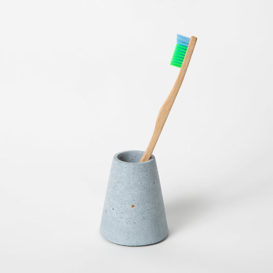 Concrete terrazzo toothbrush holder seen in light blue terrazzo holding toothbrush.